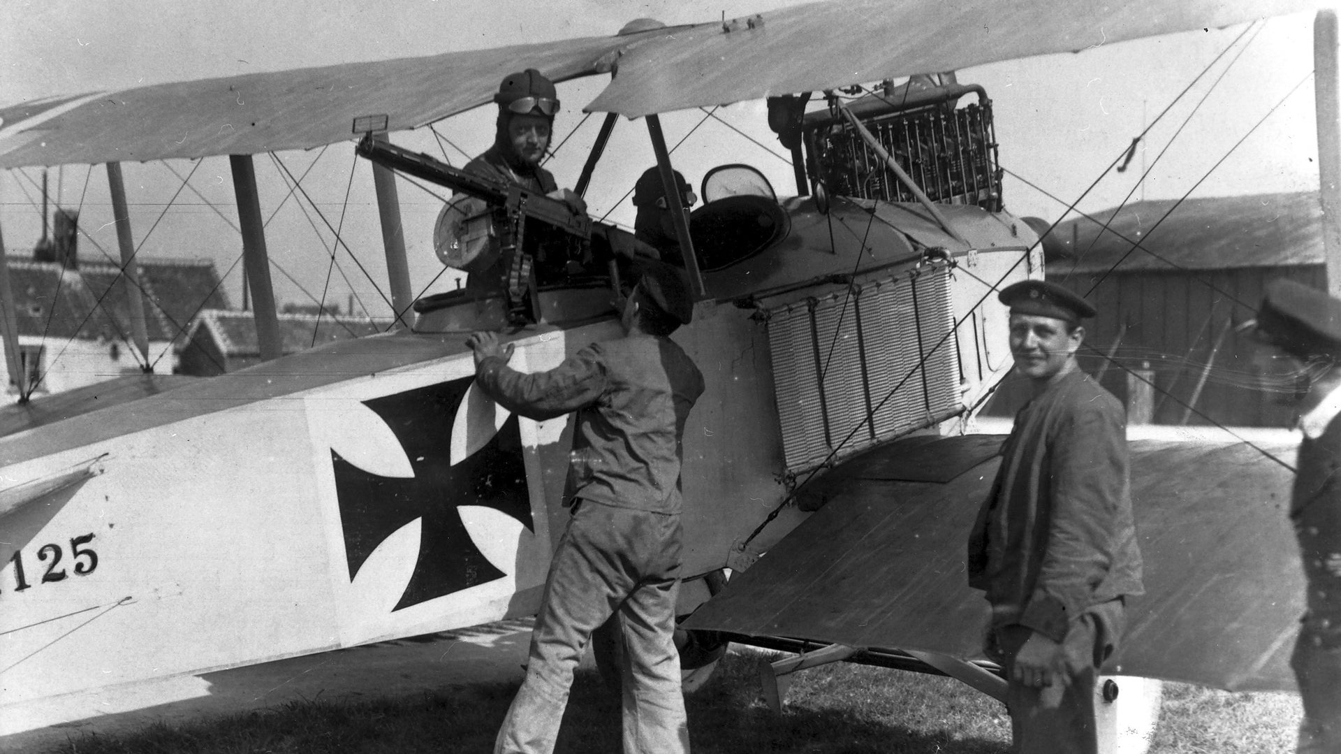 Primul Razboi Mondial: un avion de recunoastere/de lupta cu doua locuri, ilustrat pe un aerodrom naval german, in timp ce un tragator aerian verifica mitraliera.